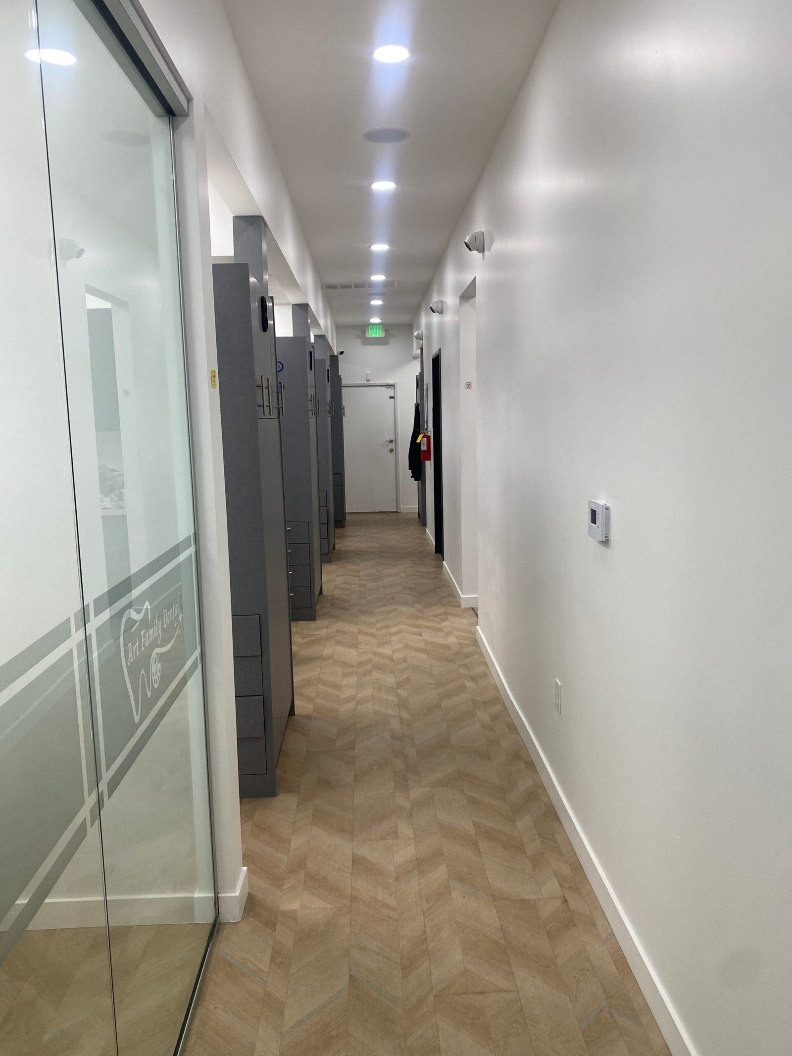 Clean, modern hallway with a wooden herringbone floor and frosted glass doors at Art Family Dental clinic.
